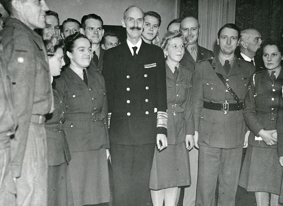 Photo taken in the Danish club at the celebration of King Christian X’s 73rd birthday. Magda Marie Andersen is standing next to King Haakon VII of Norway, and Karen Andersen is standing next to Magda. The photo also include two Danish RAF-pilots, Jørgen Herner Petersen looking over the King’s shoulder, and an unidentified volunteer standing between the King and Magda. Second from the right is Maj. Eyvind Knauer, who was in charge of the Recruiting Office, Danish Nationals from July 1943 to May 1944. Looking over his right shoulder is Lt Col Helge William Spange (O-0276655), US Army. (Museum of Danish Resistance)
